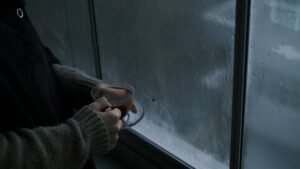 A person enjoys a cup of tea by a rainy window, exuding a calming and reflective mood.